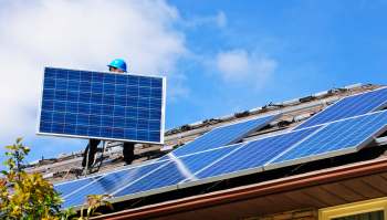 A person installs a solar panel on a roof covered with solar panels under a blue sky.