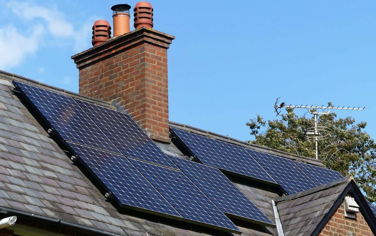 Solar panels installed on a roof with a chimney and an antenna nearby.