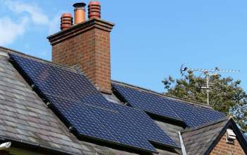 Solar panels installed on a roof with a chimney and an antenna nearby.