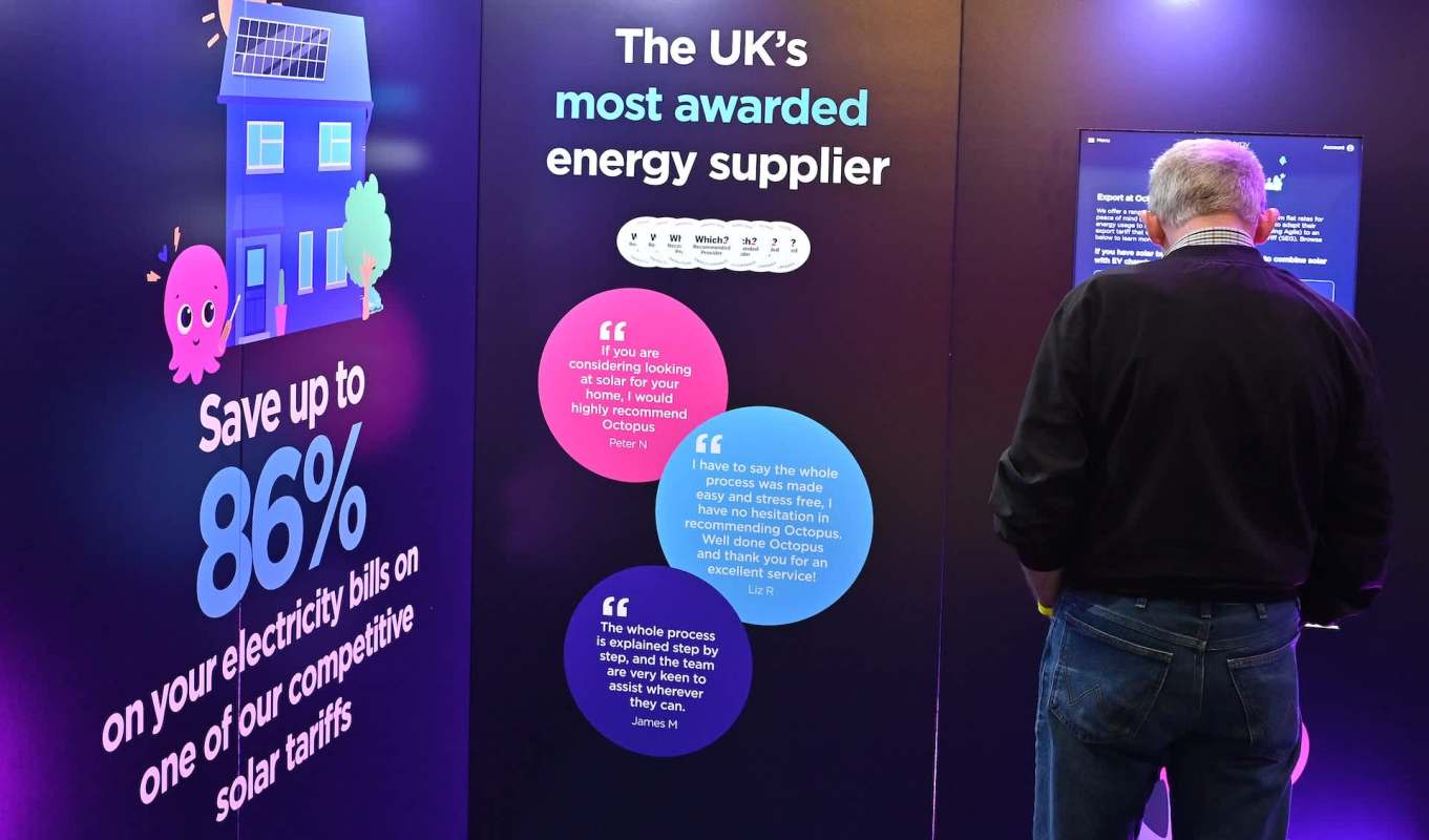 A person interacts with an Octopus Energy promotional display about energy savings and solar tariffs.