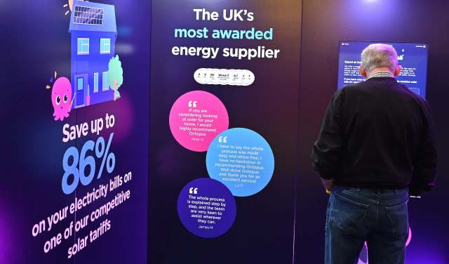 A person interacts with an Octopus Energy promotional display about energy savings and solar tariffs.