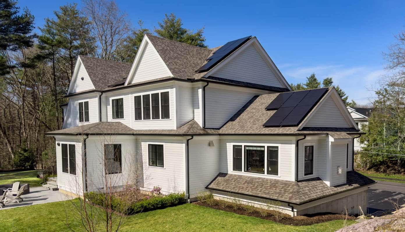A white house with solar panels on the roof, surrounded by grass and trees.