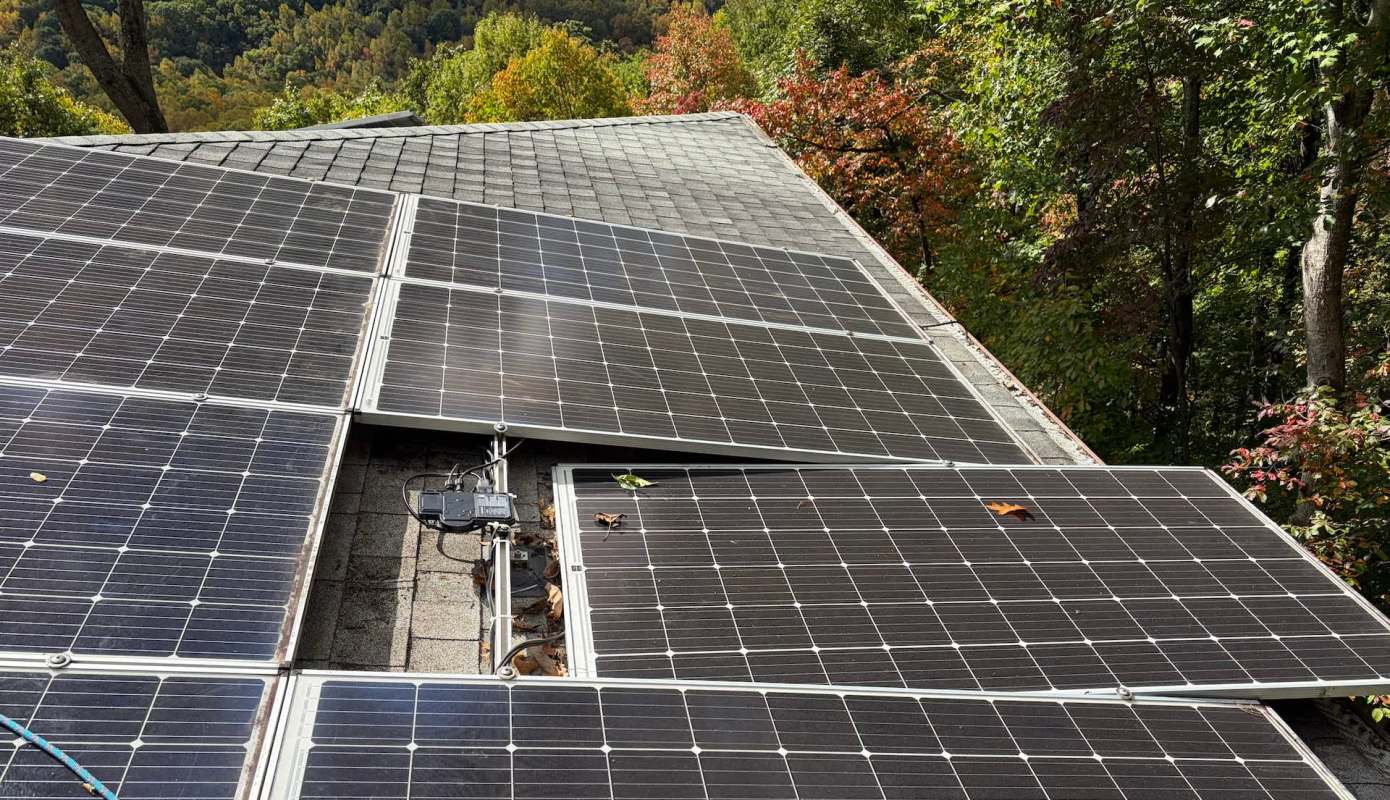 Solar panels installed on a roof, with a backdrop of trees showing autumn colors.