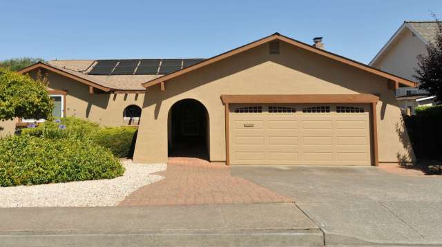 A single-story house with solar panels, a driveway, and landscaped front yard.