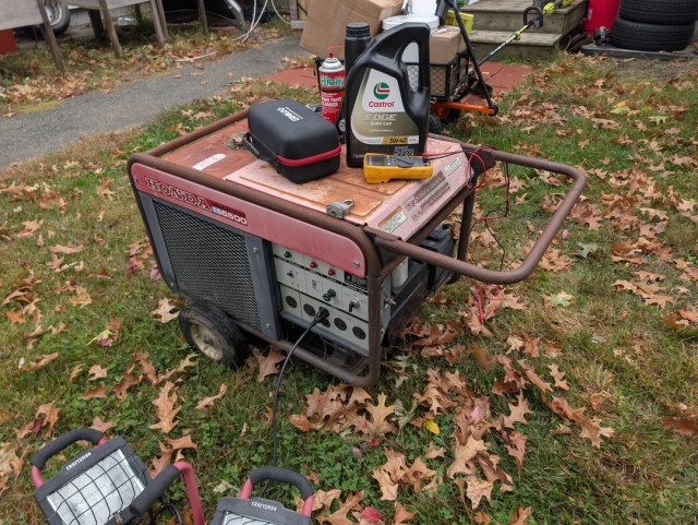 A Honda generator with tools and oil can on a lawn covered in fallen leaves.