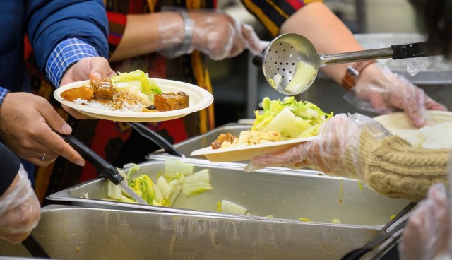 People serving food at a community meal, with plates of rice and vegetables being distributed.