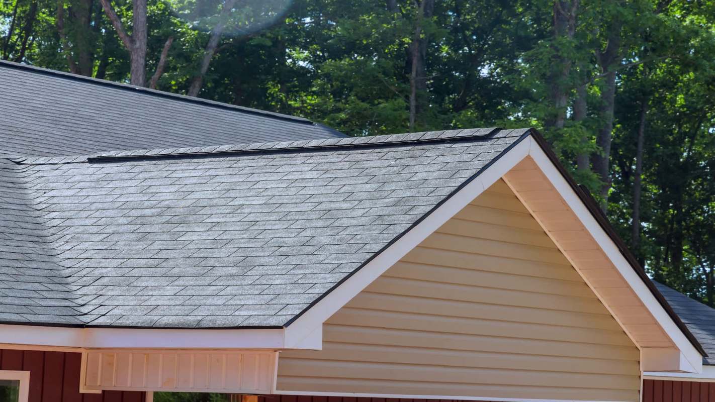 A close view of a roof with shingles and a gable end against a backdrop of trees.