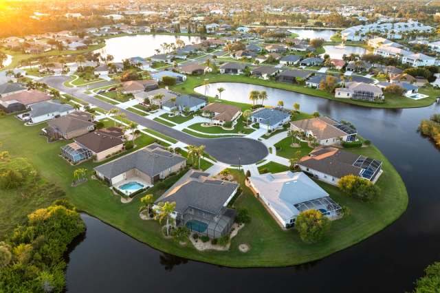 An aerial view of a suburban neighborhood with houses, streets, and a nearby pond.