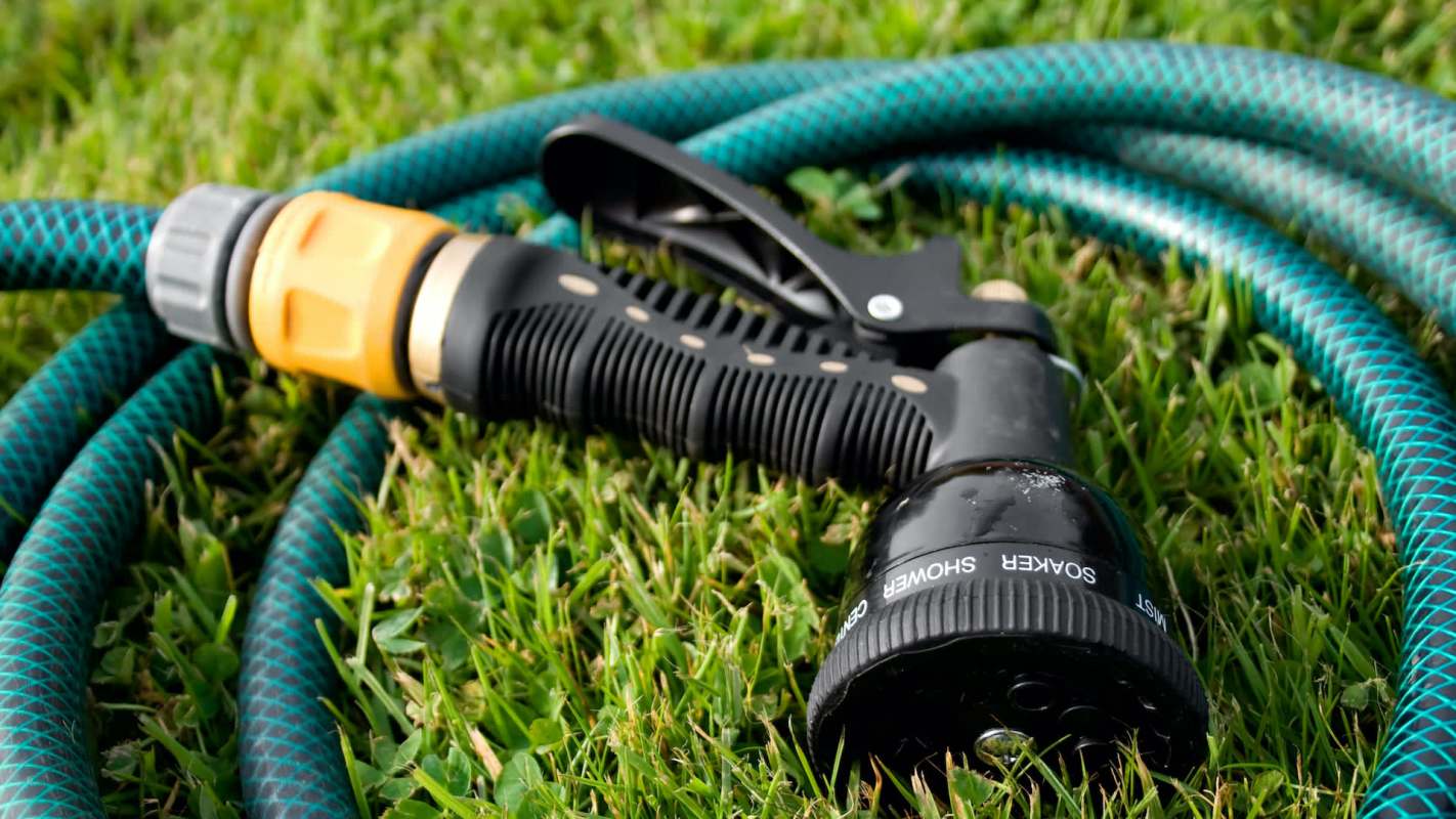 A garden hose with a spray nozzle lies on the grass.