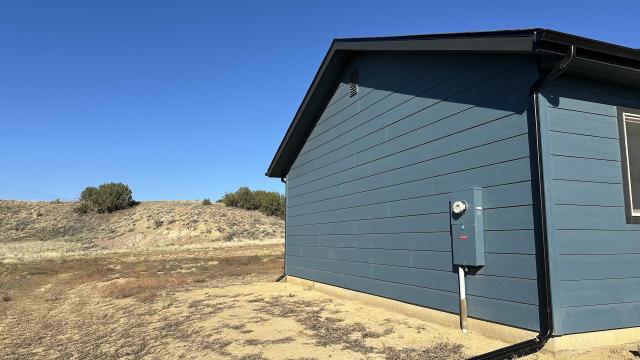 A blue house with a utility meter next to a sparse landscape under a clear blue sky.