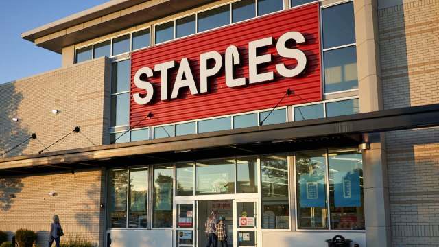 A Staples store entrance with a large red sign and customers entering.