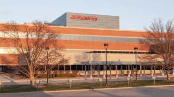 A brick building with large windows and a sign for State Farm, alongside a parking area marked for visitors.