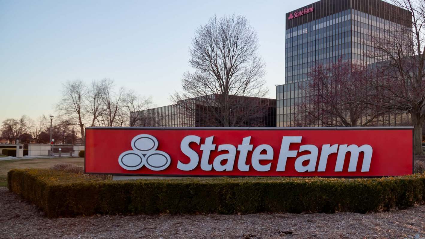 A State Farm sign in front of a building with trees and landscaping.