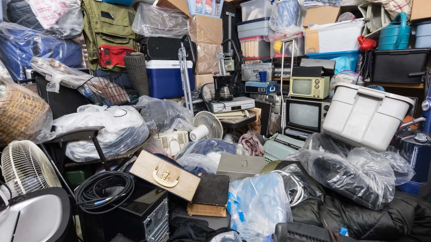 A cluttered storage space filled with various items, including bags, appliances, and furniture, all partially covered in plastic.