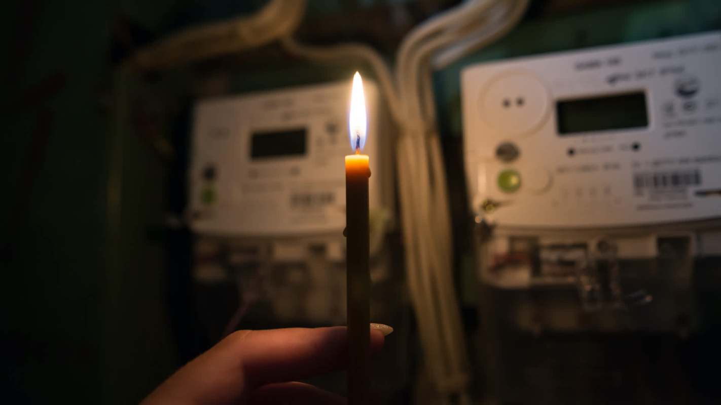 A lit candle is held in front of electrical meters in a dimly lit environment.