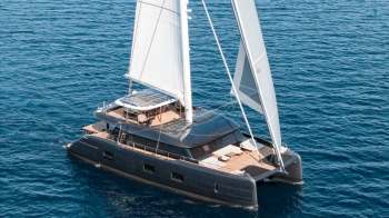A sailing catamaran with solar panels and white sails on blue water.