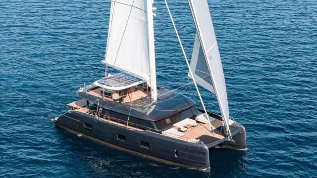 A sailing catamaran with solar panels and white sails on blue water.