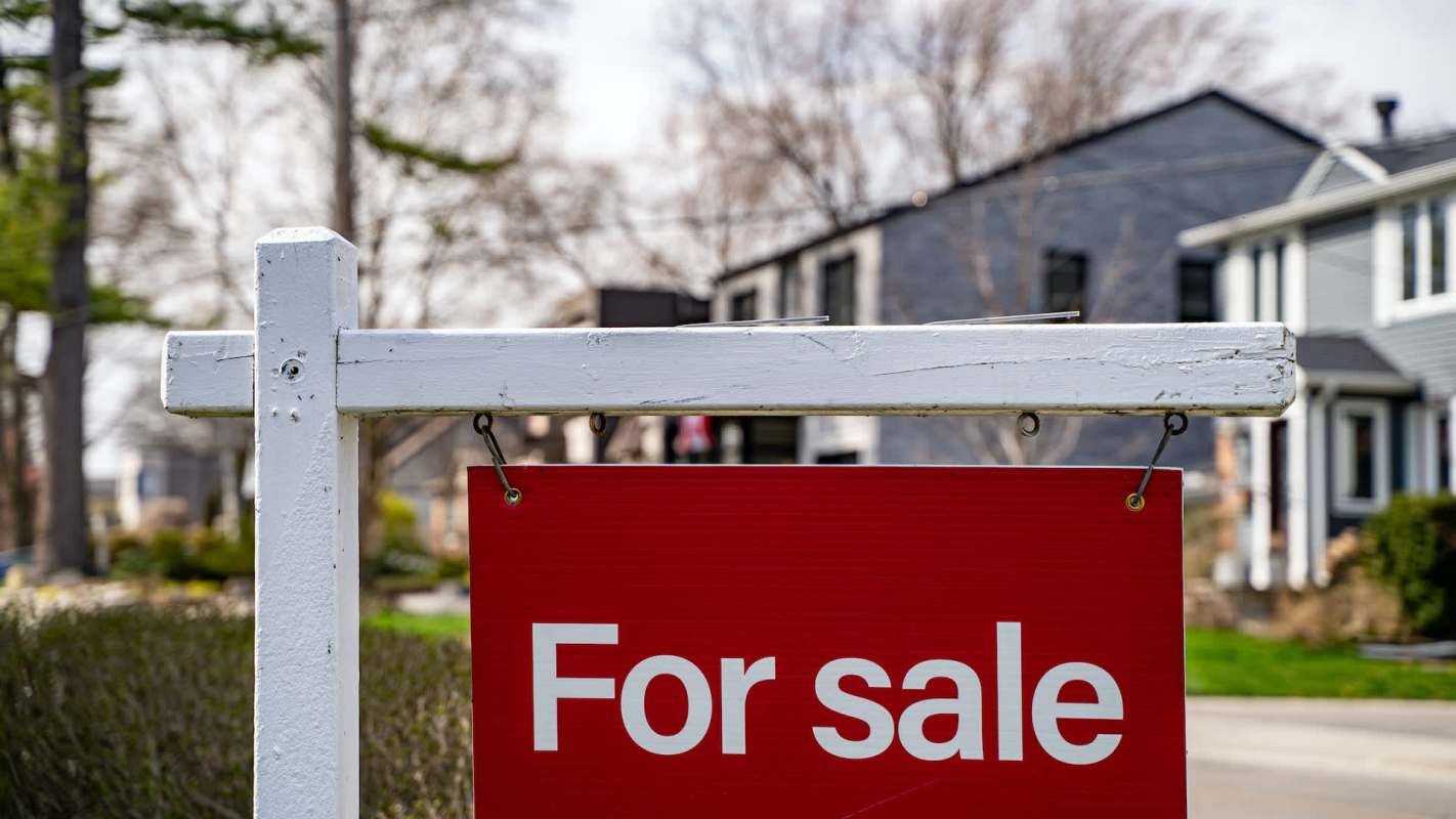 A "For Sale" sign in front of residential houses.
