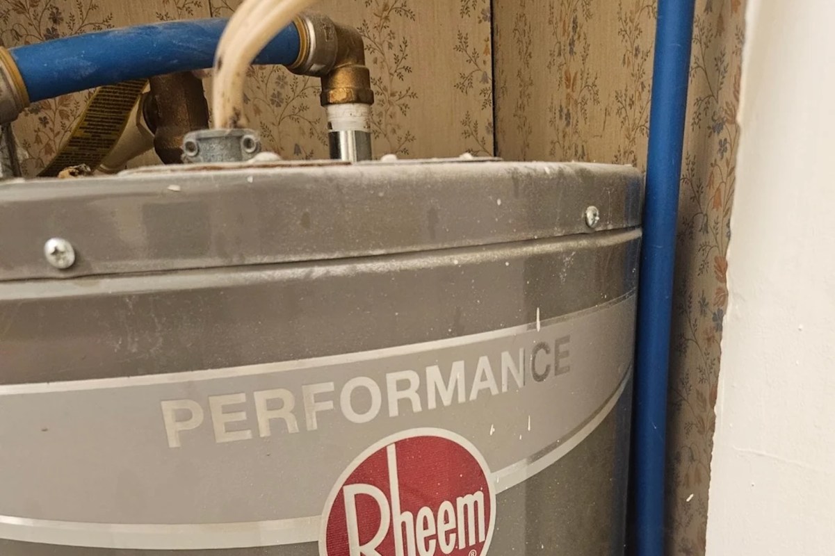 A water heater with visible pipes and a floral wallpaper background.