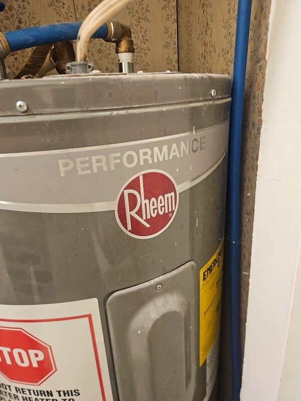 A water heater with visible pipes and a floral wallpaper background.