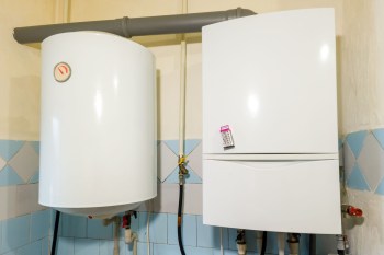 A white water heater and a white storage boiler mounted on a wall with blue tiled accents.