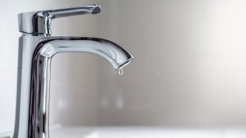 A modern faucet with a single drop of water hanging from the spout.