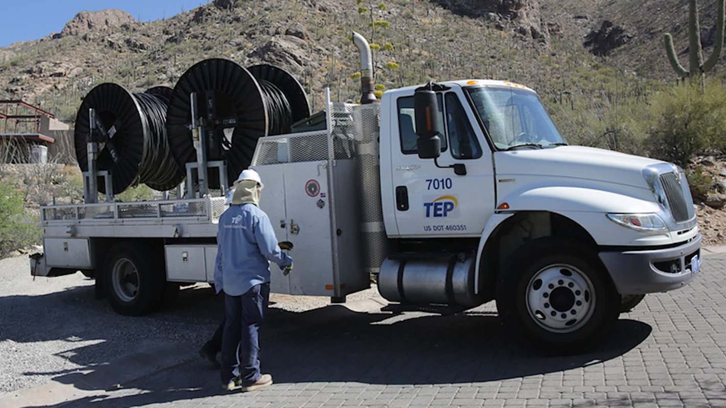 A truck carrying large spools of cable is parked in a desert area with mountains in the background.