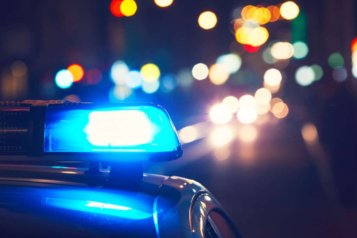 A police car's blue emergency light illuminated at night with blurred city lights in the background.