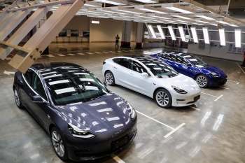 Three Tesla cars in a modern indoor parking area, featuring gray, white, and blue models.