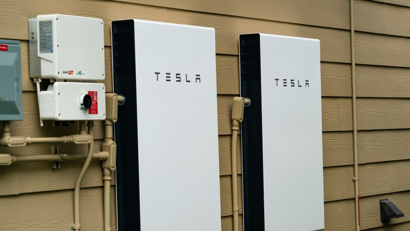 Two Tesla home battery units mounted on a wall next to electrical equipment and plumbing.