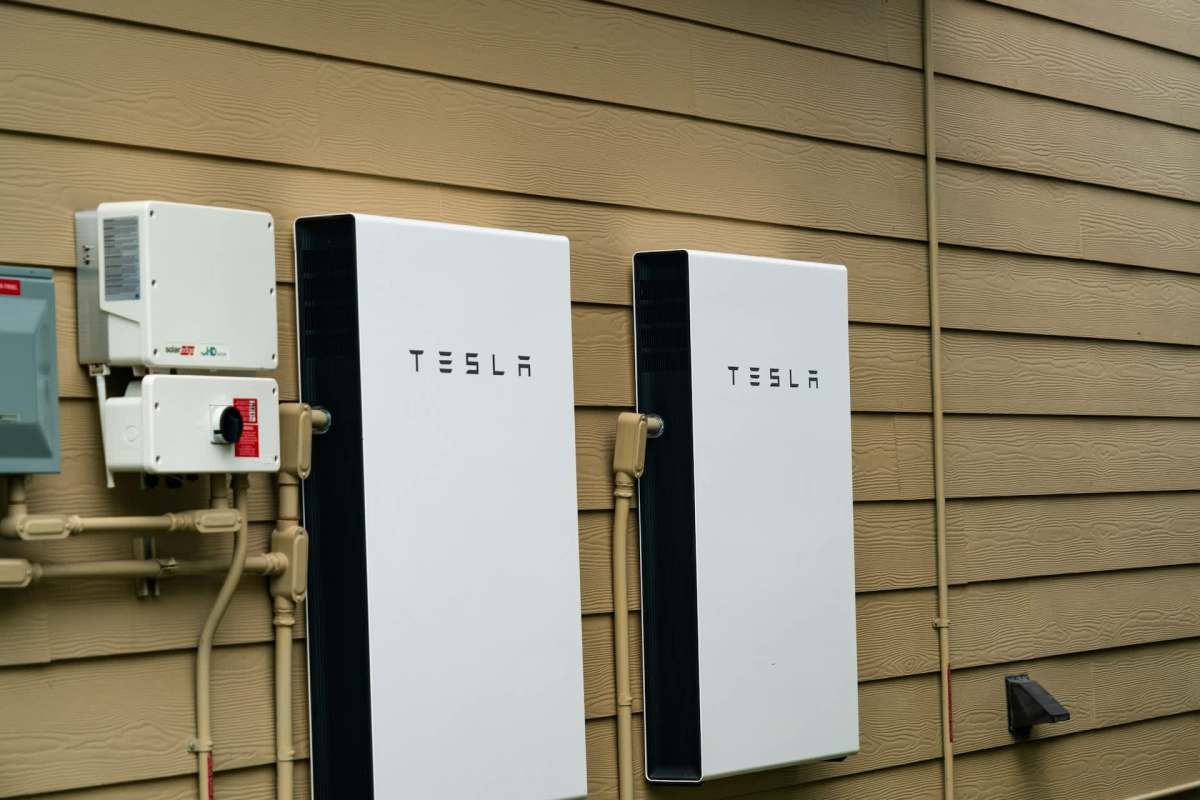 Two Tesla energy storage units mounted on a wall next to electrical equipment.