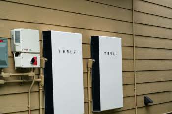 Two Tesla energy storage units mounted on a wall next to electrical equipment.