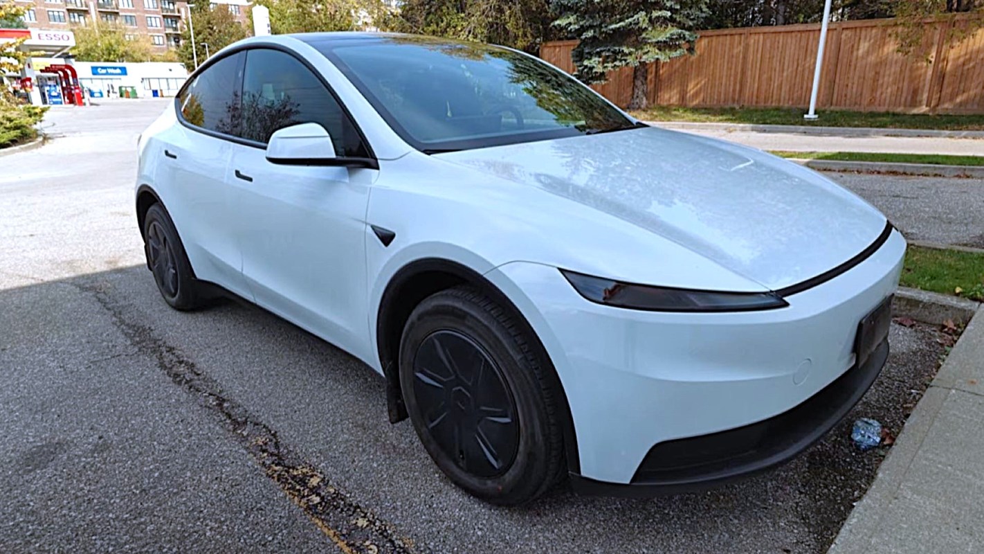 A white electric car parked on a paved surface near a gas station.