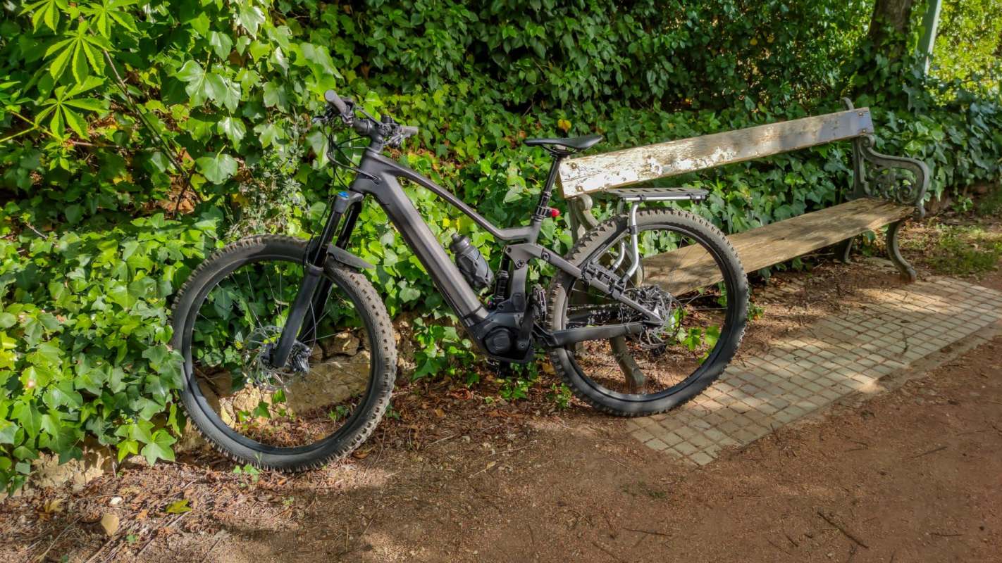 An e-bike next to a wooden bench on a dirt trail.