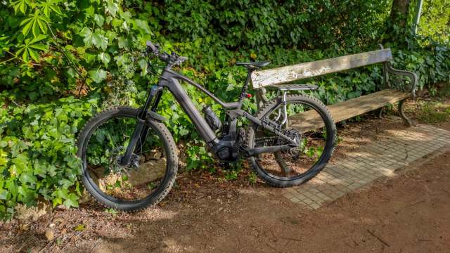 An e-bike next to a wooden bench on a dirt trail.