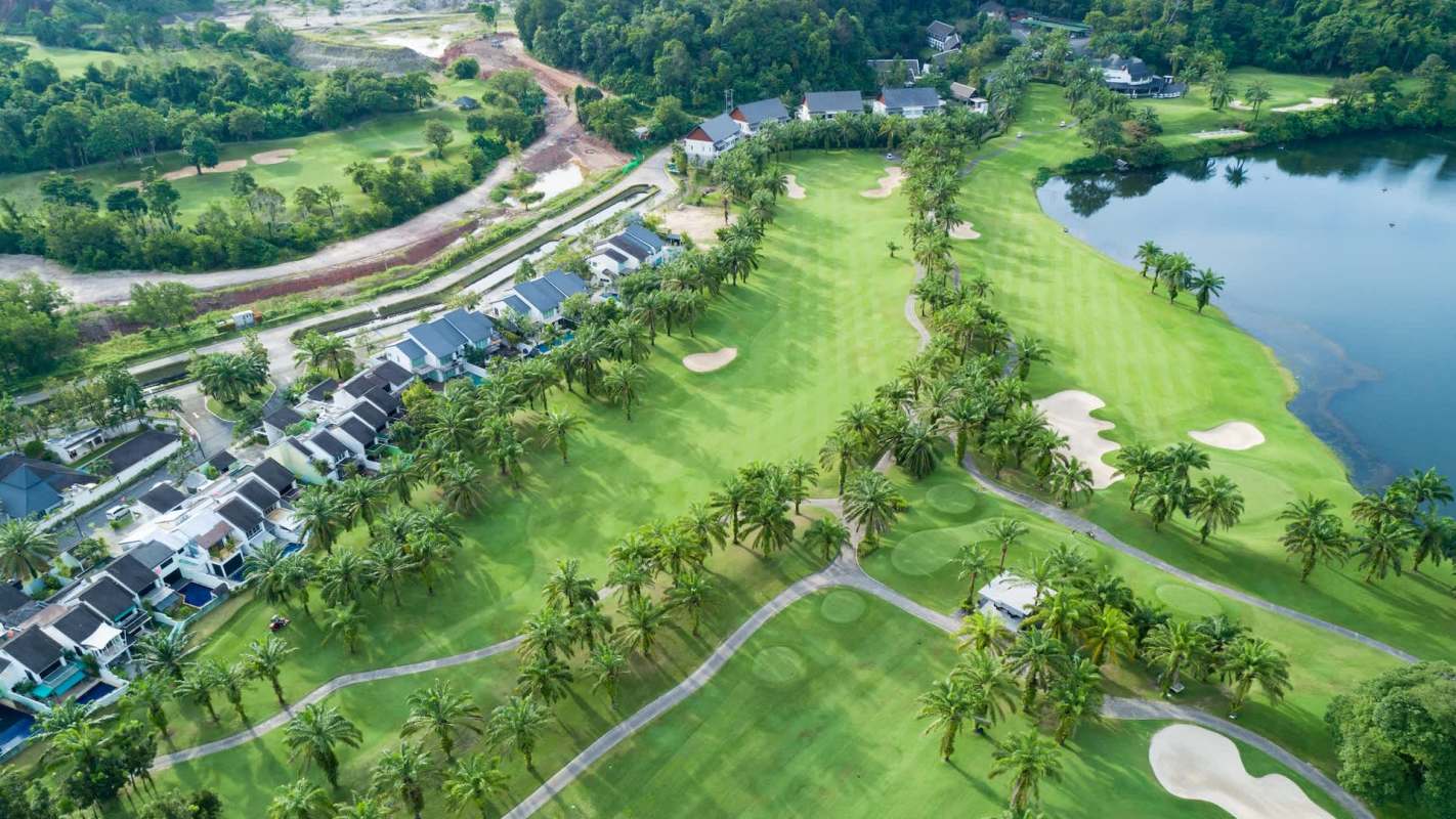 Aerial view of a golf course with palm trees, residential buildings, and a surrounding lake.