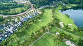 Aerial view of a golf course with palm trees, residential buildings, and a surrounding lake.