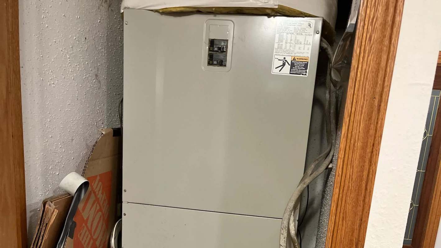 A water heater positioned in a narrow utility space next to cardboard boxes and exposed pipes.