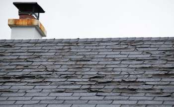 A roof with damaged and peeling shingles, featuring a chimney with a rusted cap.