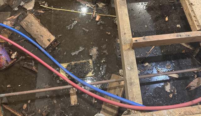 A flooded area with water, debris, wood pieces, and two hoses running across the floor.