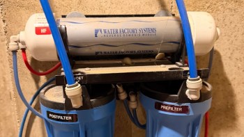 A reverse osmosis water filtration system with blue pipes and filters labeled "POSTFILTER" and "PREFILTER."