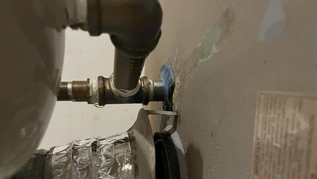 A metallic pipe connection on a water heater with a valve, showing a green stain from a blue plastic piece.
