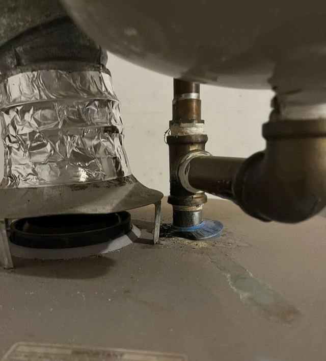 A metallic pipe connection on a water heater with a valve, showing a green stain from a blue plastic piece.