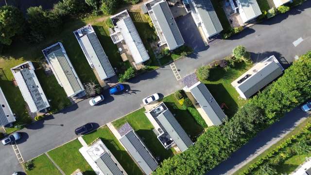 An aerial view of a row of mobile homes along a paved road surrounded by greenery.