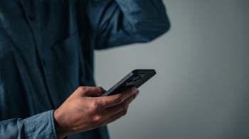A person holding a smartphone while standing against a plain background.
