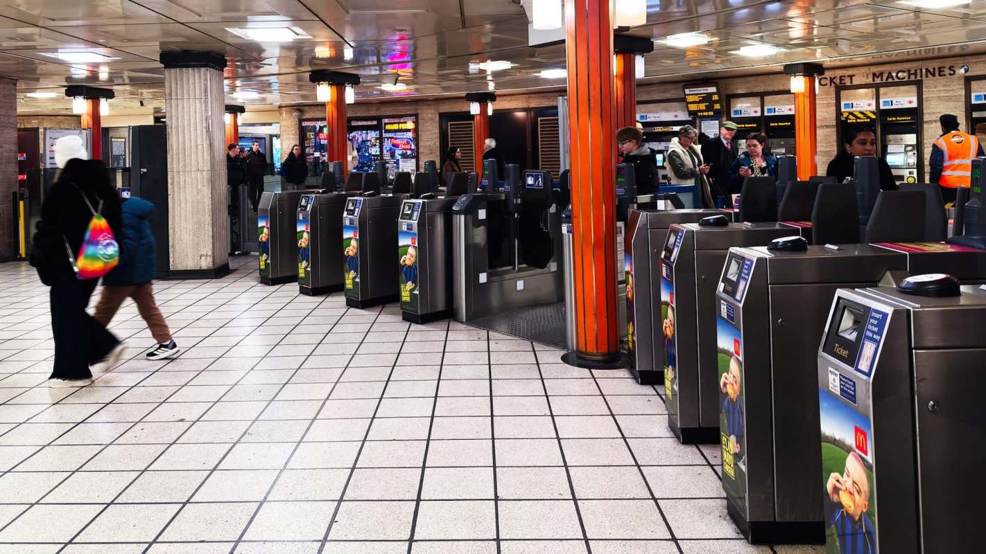 A busy London subway station with ticket machines and passengers walking between turnstiles.