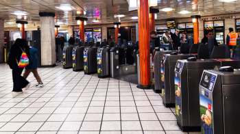 A busy London subway station with ticket machines and passengers walking between turnstiles.