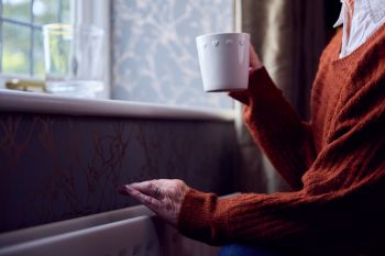 A woman enjoying a hot drink while standing near a radiator.