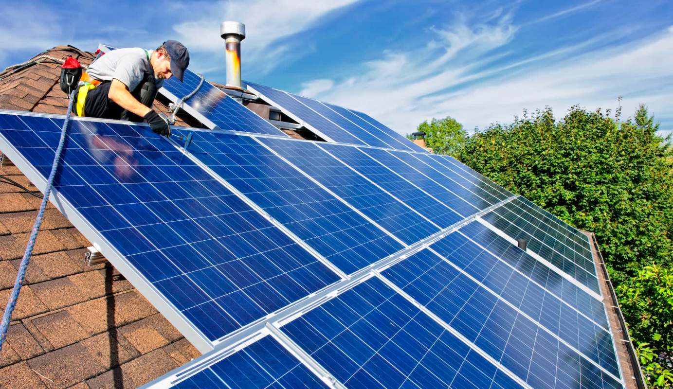 A person working on solar panels installed on a roof under a clear blue sky.
