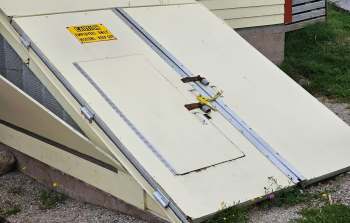 A locked access door with a caution sign on a ramp outside a building.
